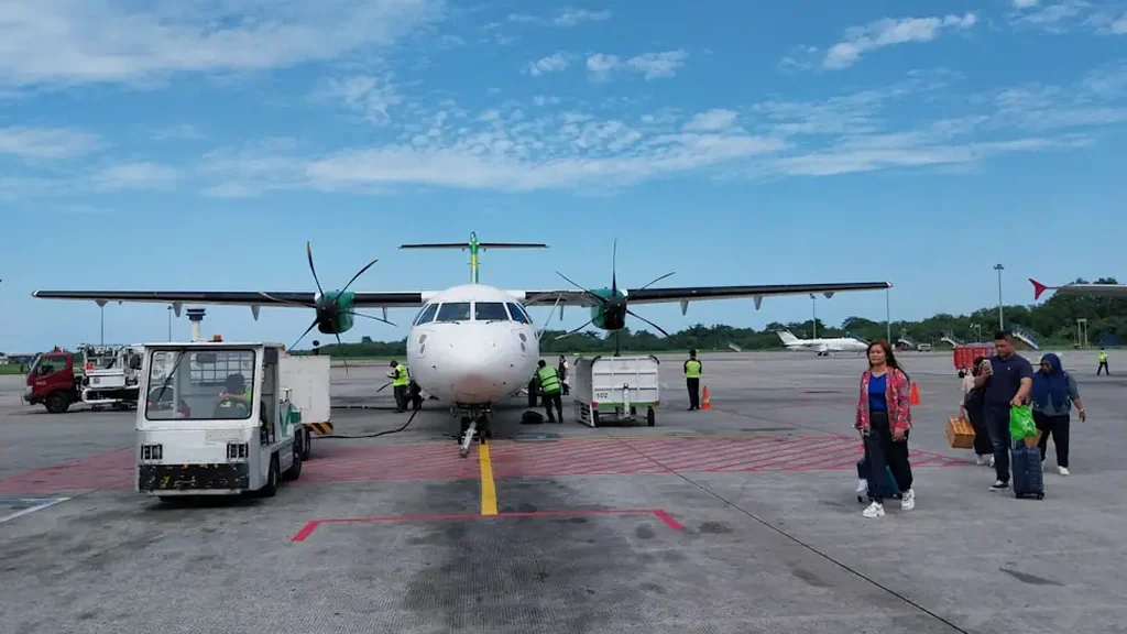 A turboprop airliner parked on an airport apron while passengers walk across the tarmac with their luggage