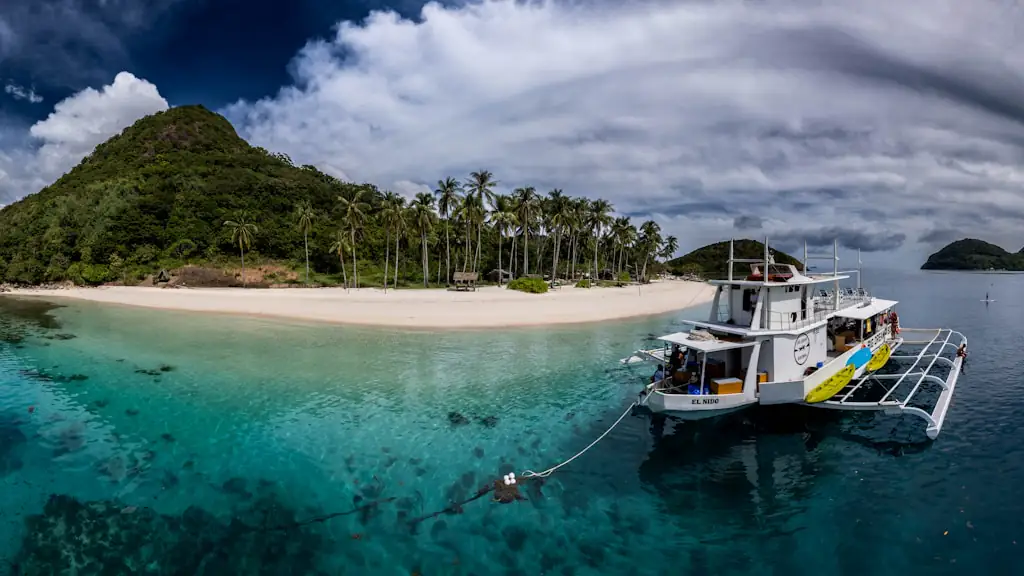 An outrigger passenger boat anchored off a palm-fringed white-sand island in clear turquoise water