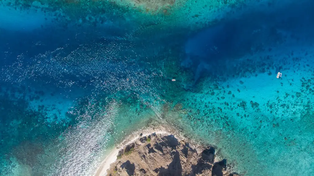 Overhead aerial view of a rocky headland, white sand beach and turquoise reef shallows with small boats offshore