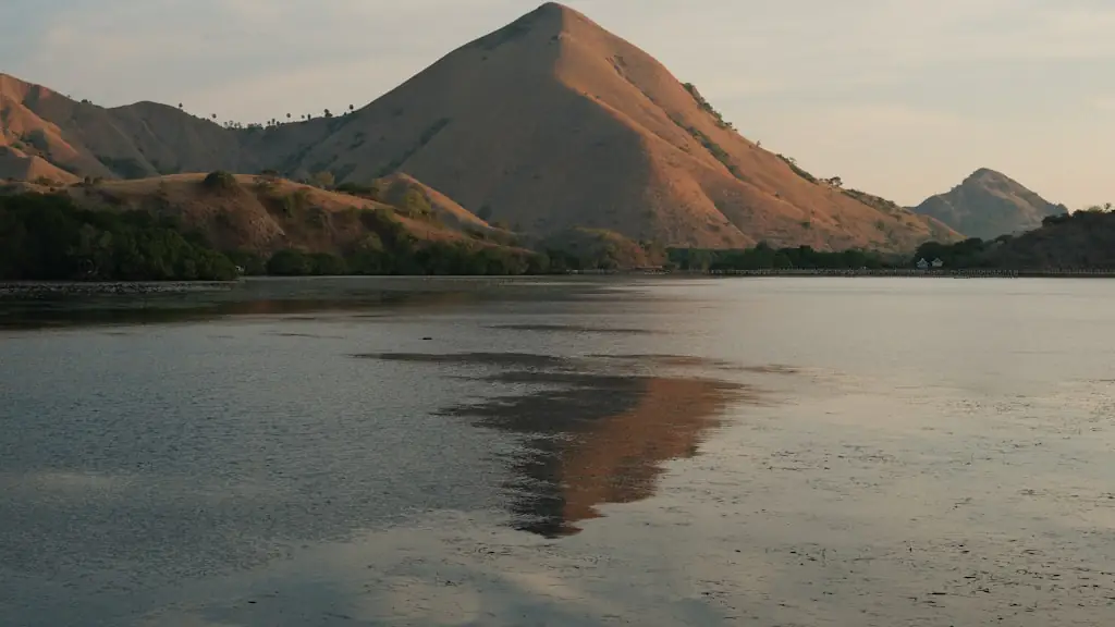 Bare golden-brown hills reflected in the still water of a sheltered bay in low light