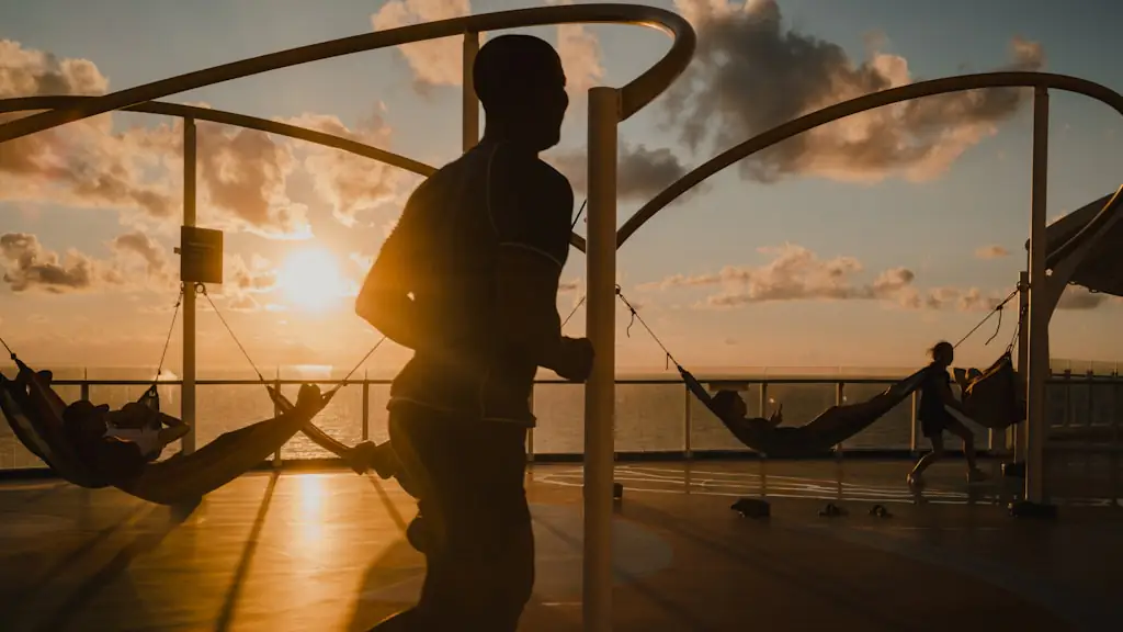 A person silhouetted on a boat deck strung with hammocks as the sun sets over the water