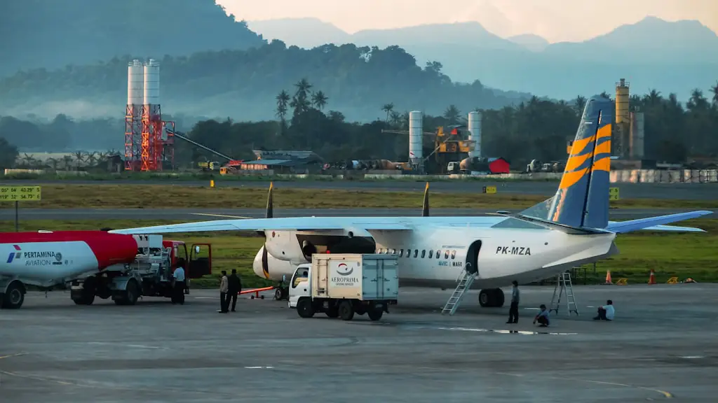 Airliner parked at an apron with refuelling and service vehicles, misty forested mountains behind