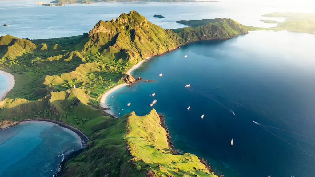 Aerial view of a green island ridge beside a deep blue bay with small boats on the water