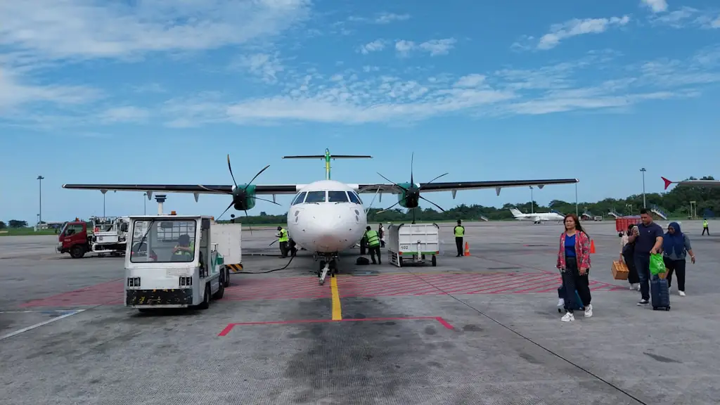 Turboprop airliner parked on an airport apron while passengers walk across the tarmac with their luggage