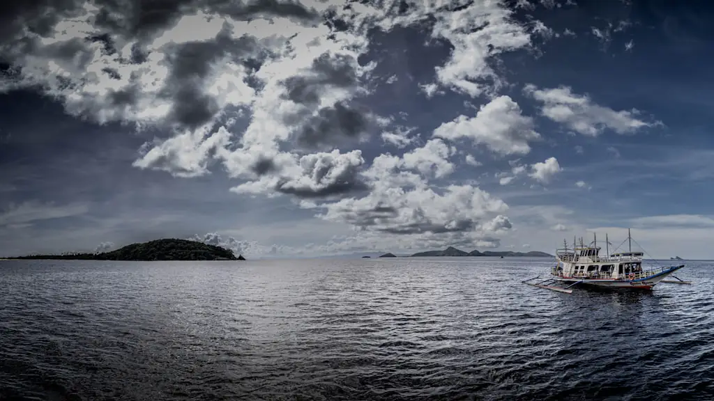 A wooden outrigger tour boat on open water beside a low forested islet under heavy cloud