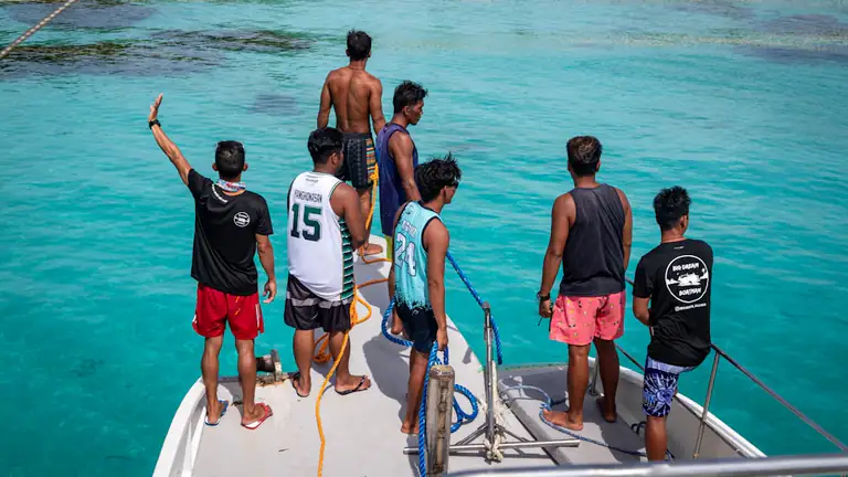 Group of young men standing at the bow of a small boat over clear turquoise water near a reef