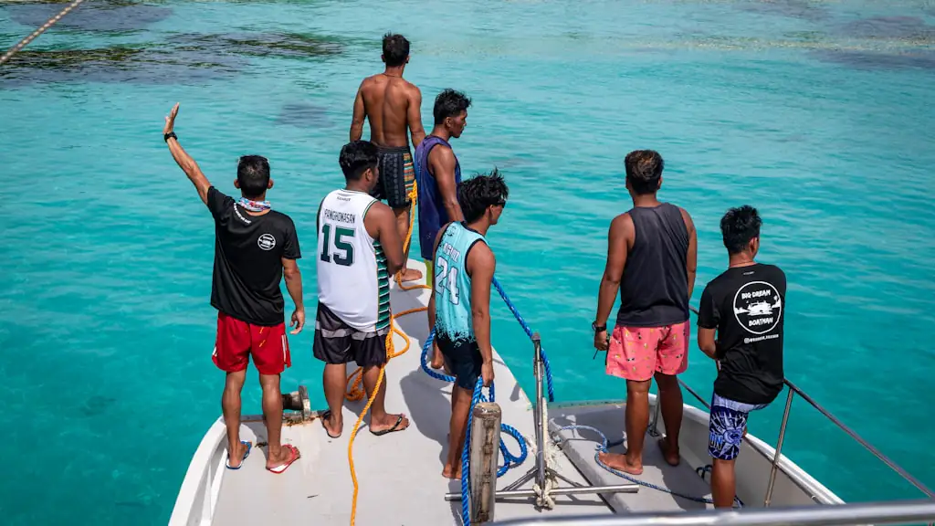 Group of young men standing at the bow of a small boat over clear turquoise water near a reef
