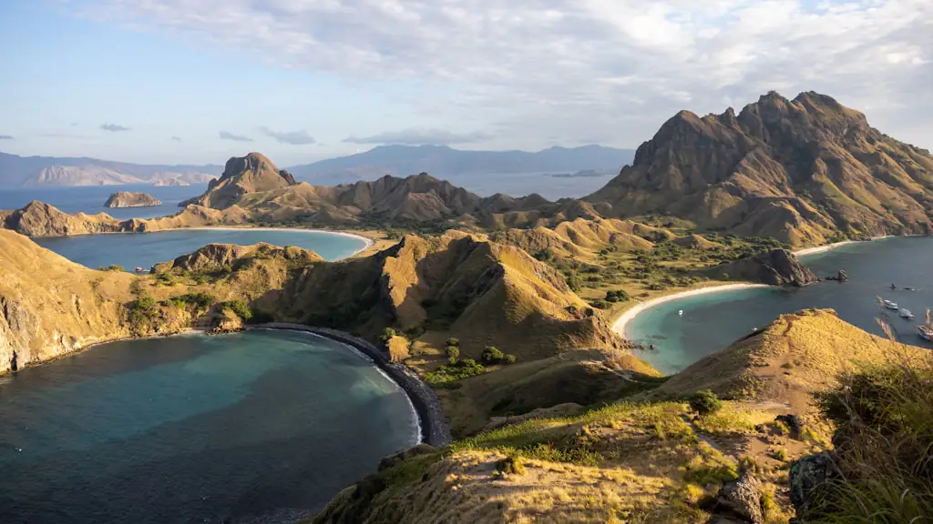 Aerial view of dry ridges and curving sand beaches enclosing two deep bays under a cloudy sky