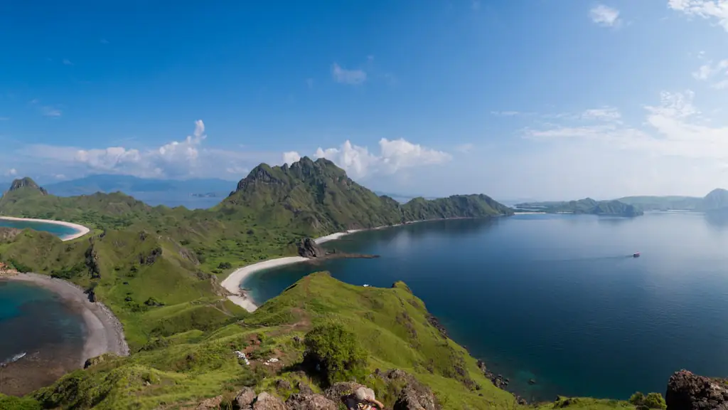 View from the Padar Island summit ridge looking down over curving bays, white-sand beaches and green ridges, with rocky ground in the foreground