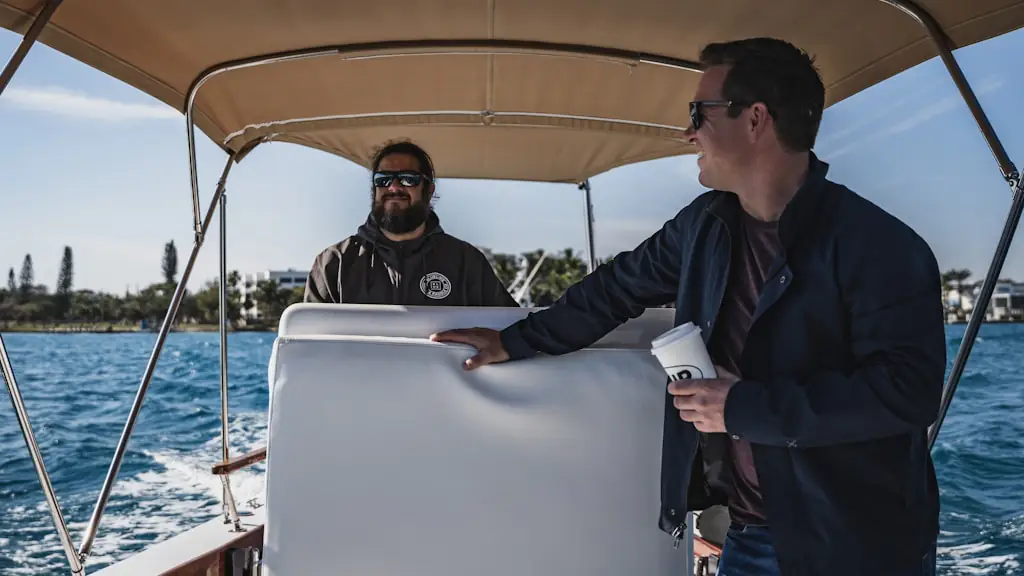 Two men at the helm console of a small boat under a canvas canopy as it crosses open water