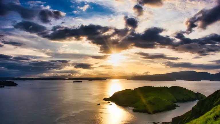 Sunset over a bay with a green headland and distant islands, seen from a hilltop viewpoint