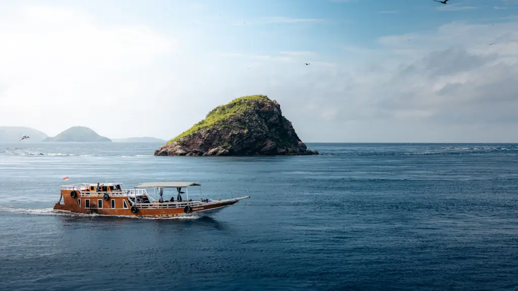A wooden tour boat crossing deep blue open water past a small steep-sided island
