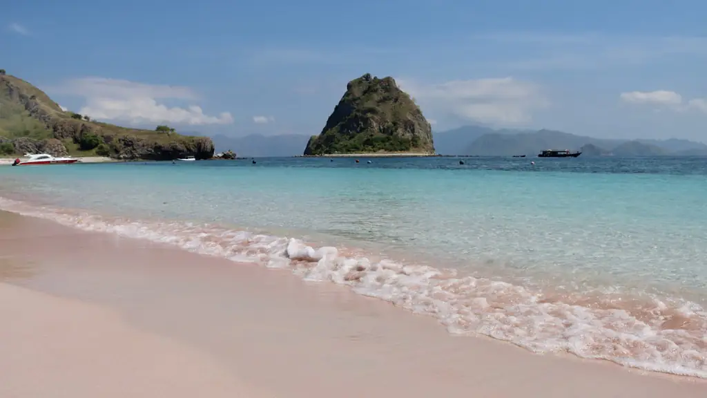 Pale pink-tinted sand beach with clear shallow water and a rocky headland offshore