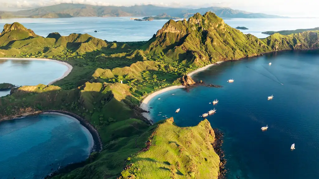 Aerial view of bright green island ridges in low golden light, above curved sand beaches with boats moored in the bays below